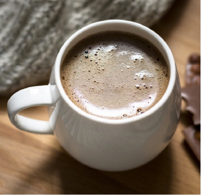 Hot chocolate served in a rounded white ceramic mug with rich froth on a wooden table.