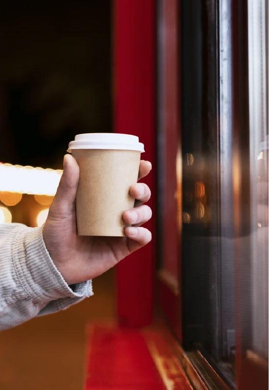 Premium Coffee and Tea takeaway cup held by a hand offering authentic tea in syria near a warm cafe window.
